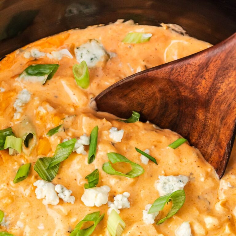 buffalo chicken dip in crock pot garnished with thinly sliced green onions and chunks of bleu cheese